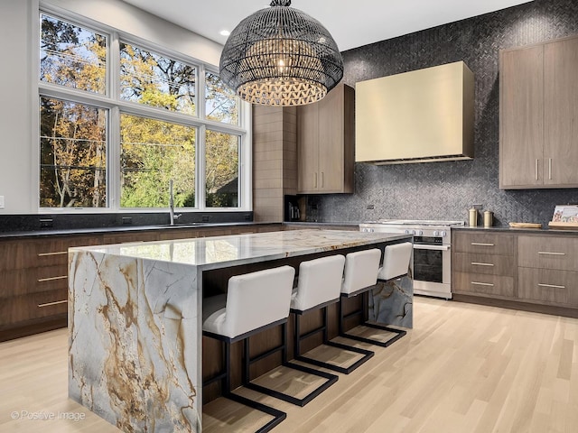 kitchen featuring light stone countertops, high end stove, decorative light fixtures, a kitchen island, and exhaust hood