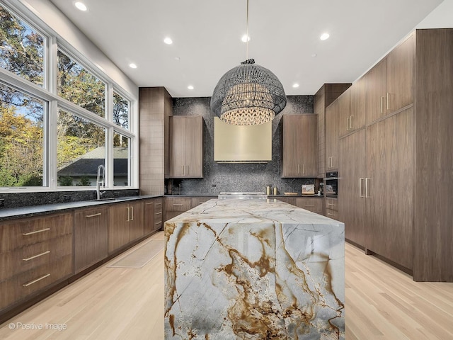 kitchen featuring sink, dark stone countertops, pendant lighting, decorative backsplash, and light wood-type flooring