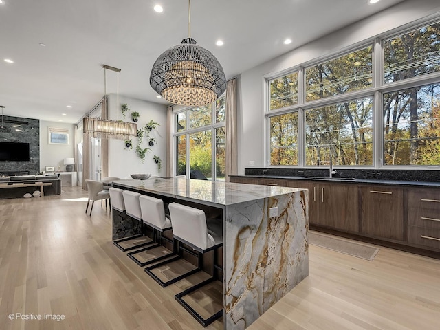 kitchen featuring sink, hanging light fixtures, dark stone counters, a breakfast bar area, and light wood-type flooring