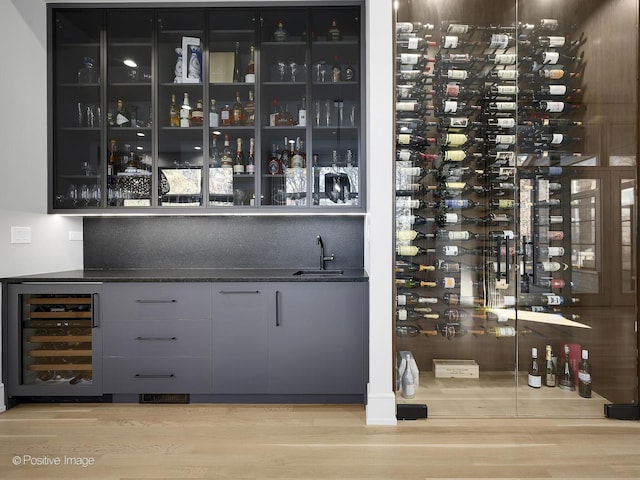 wine area with electric panel, light hardwood / wood-style floors, wet bar, and beverage cooler