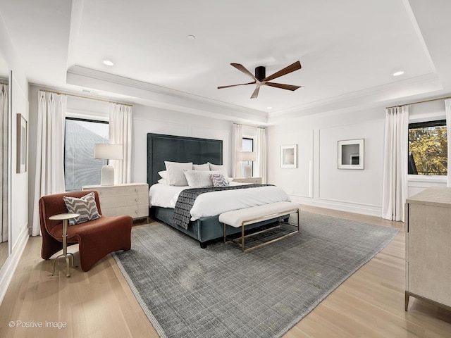 bedroom with light hardwood / wood-style flooring, a raised ceiling, ceiling fan, and crown molding