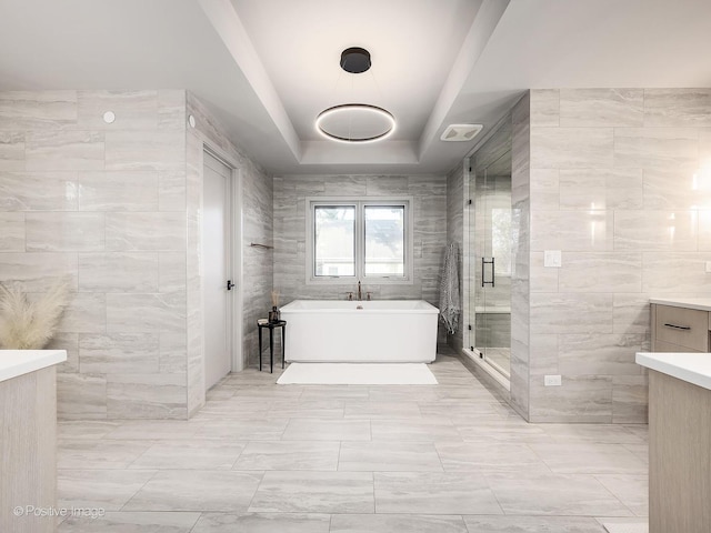 bathroom with a raised ceiling, vanity, independent shower and bath, and tile walls