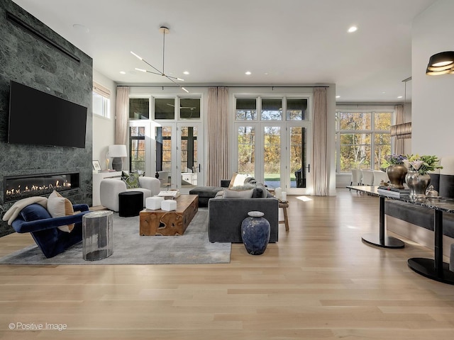 living room featuring a healthy amount of sunlight, light wood-type flooring, a premium fireplace, and a chandelier