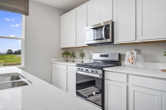 kitchen featuring sink, stainless steel appliances, white cabinetry, and light stone counters