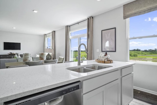 kitchen with light stone countertops, white cabinets, sink, dishwasher, and hardwood / wood-style floors