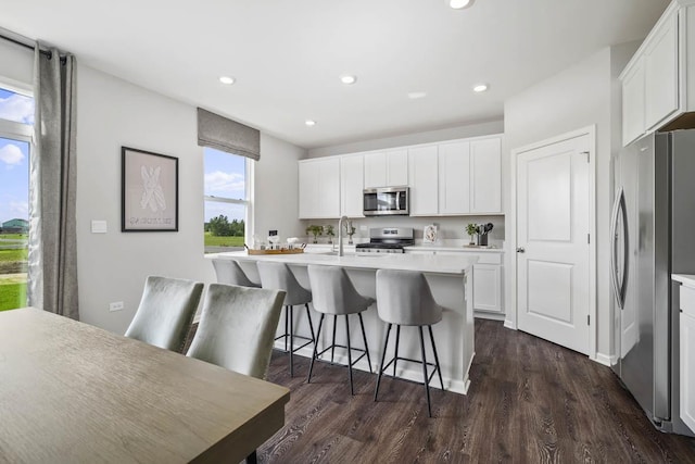 kitchen featuring a kitchen bar, appliances with stainless steel finishes, a center island with sink, white cabinets, and dark hardwood / wood-style floors