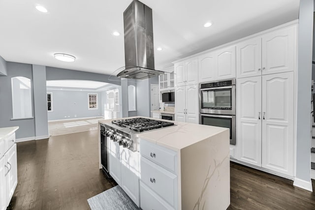 kitchen featuring light stone counters, white cabinets, island range hood, and appliances with stainless steel finishes