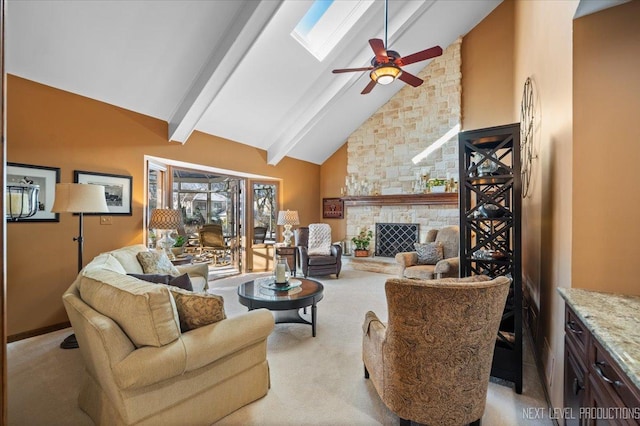 living room featuring a skylight, ceiling fan, a stone fireplace, beamed ceiling, and light colored carpet