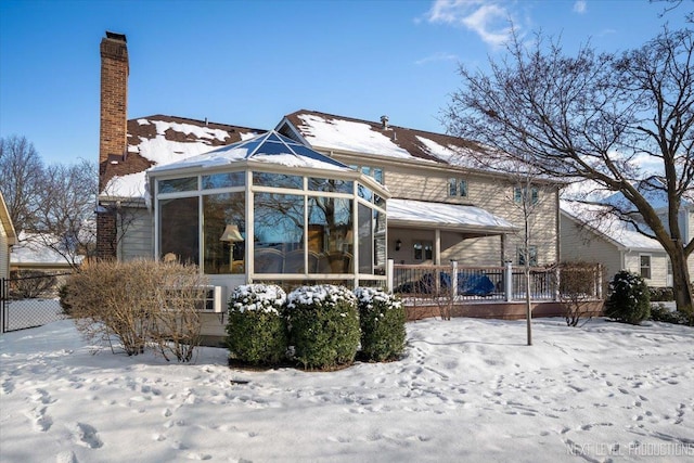 snow covered rear of property with a sunroom