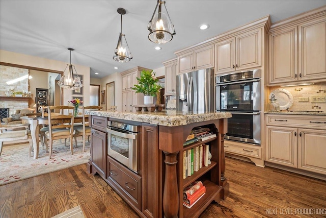 kitchen with pendant lighting, dark hardwood / wood-style floors, light stone countertops, appliances with stainless steel finishes, and a kitchen island