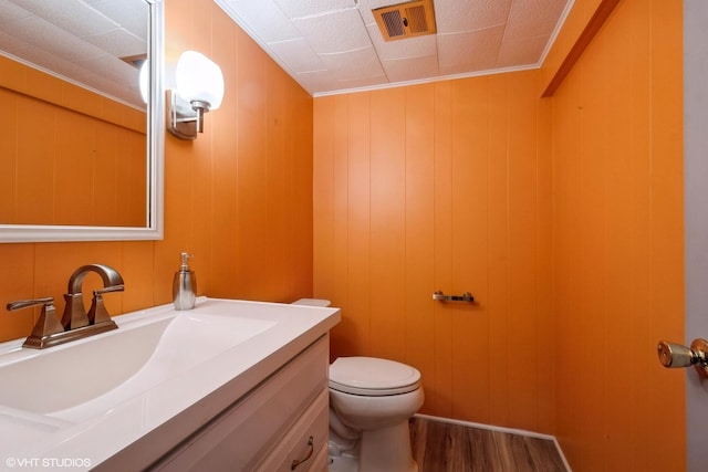 bathroom featuring hardwood / wood-style floors, vanity, wood walls, toilet, and ornamental molding