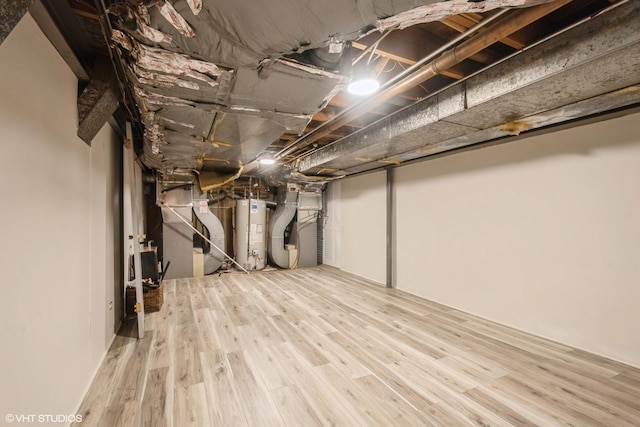 basement featuring light wood-type flooring, heating unit, and water heater