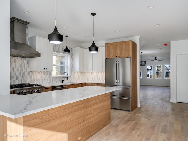 kitchen featuring ceiling fan, wall chimney exhaust hood, decorative light fixtures, white cabinets, and appliances with stainless steel finishes