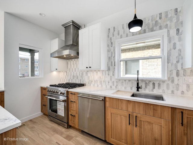 kitchen with pendant lighting, wall chimney range hood, sink, white cabinetry, and stainless steel appliances