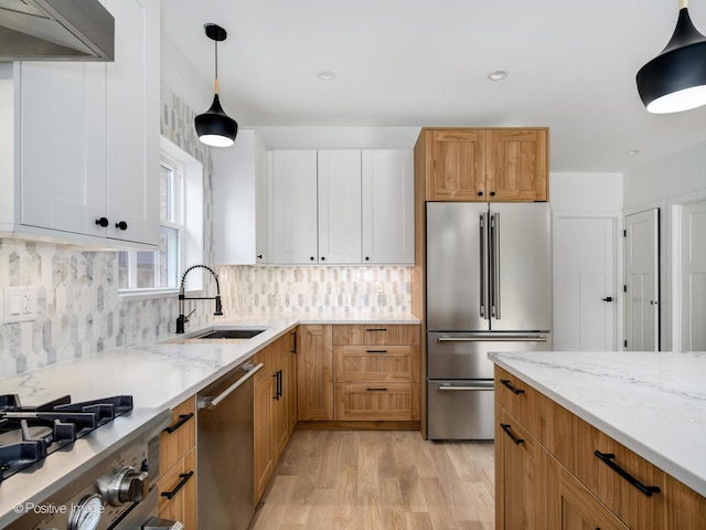 kitchen with appliances with stainless steel finishes, extractor fan, sink, white cabinets, and hanging light fixtures