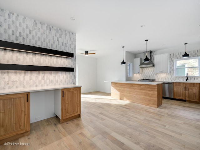 kitchen featuring stainless steel appliances, ceiling fan, sink, wall chimney range hood, and light hardwood / wood-style flooring