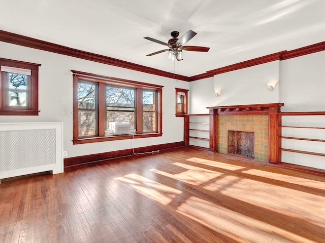 unfurnished living room with radiator, ornamental molding, ceiling fan, a tile fireplace, and hardwood / wood-style flooring