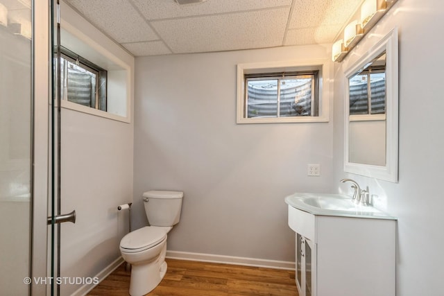 bathroom with hardwood / wood-style flooring, a drop ceiling, toilet, and vanity