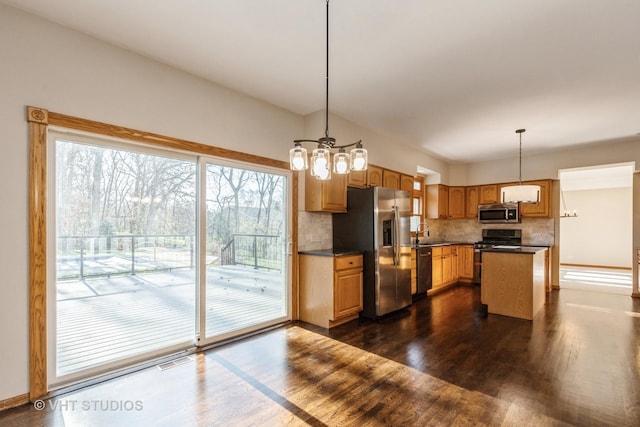 kitchen with tasteful backsplash, stainless steel appliances, sink, decorative light fixtures, and a center island