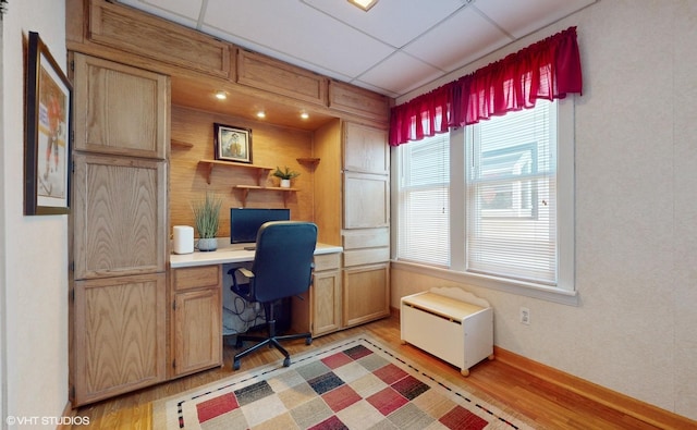 home office with built in desk, light hardwood / wood-style floors, and a drop ceiling