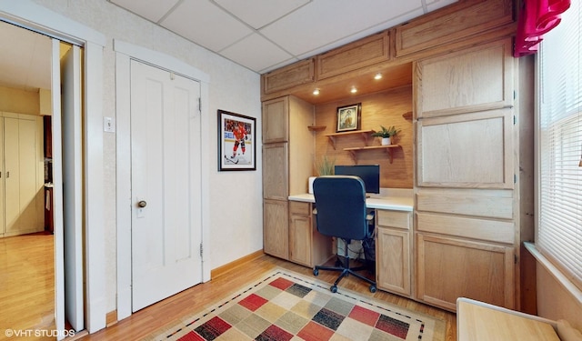 office with a paneled ceiling, built in desk, and light hardwood / wood-style floors