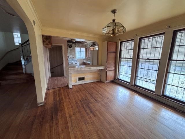 unfurnished living room featuring a healthy amount of sunlight, crown molding, a chandelier, and dark hardwood / wood-style floors