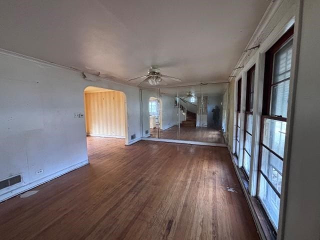 unfurnished living room featuring a healthy amount of sunlight, ceiling fan, dark wood-type flooring, and ornamental molding