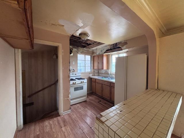 kitchen with tile countertops, ornamental molding, white appliances, and hardwood / wood-style flooring