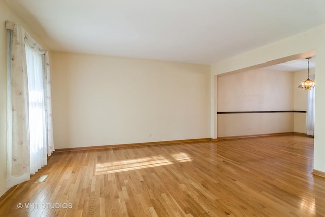 empty room featuring an inviting chandelier and light wood-type flooring