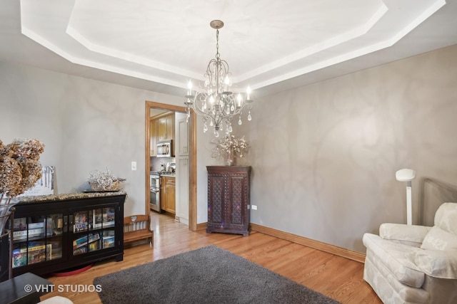 sitting room with a chandelier, a tray ceiling, and light hardwood / wood-style floors