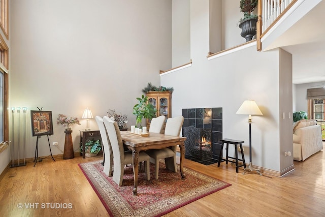 dining area featuring a tile fireplace, a towering ceiling, and light hardwood / wood-style floors