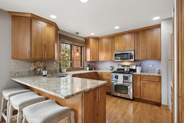 kitchen with sink, hanging light fixtures, stainless steel appliances, light stone counters, and light hardwood / wood-style flooring