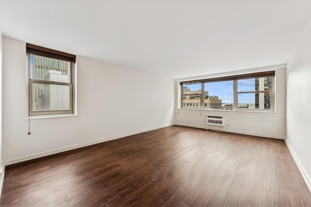 spare room with dark wood-type flooring, a wall unit AC, and baseboards