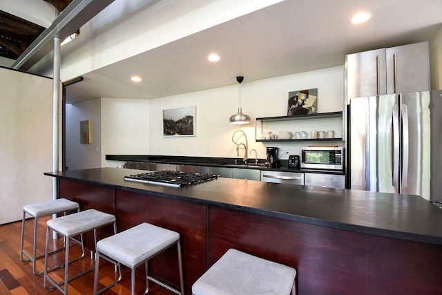 kitchen with a kitchen bar, decorative light fixtures, stainless steel appliances, and dark wood-type flooring