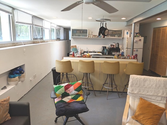 kitchen featuring a kitchen bar, ceiling fan, white cabinets, and white fridge