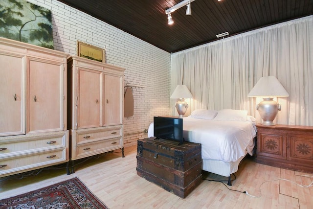 bedroom with wooden ceiling, rail lighting, brick wall, and light hardwood / wood-style flooring