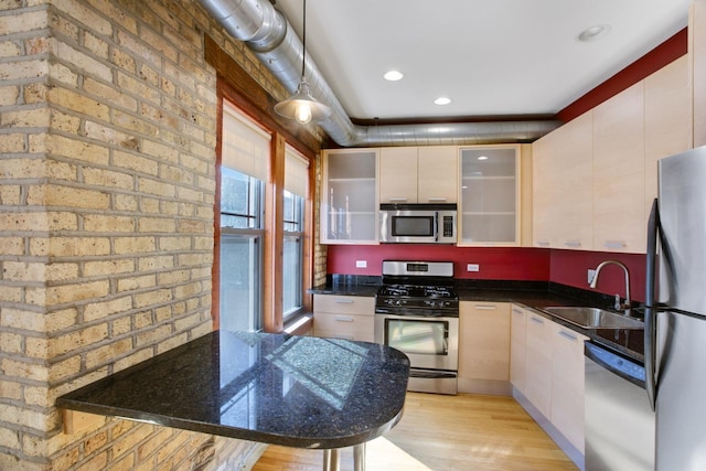 kitchen with sink, hanging light fixtures, stainless steel appliances, dark stone counters, and light hardwood / wood-style floors