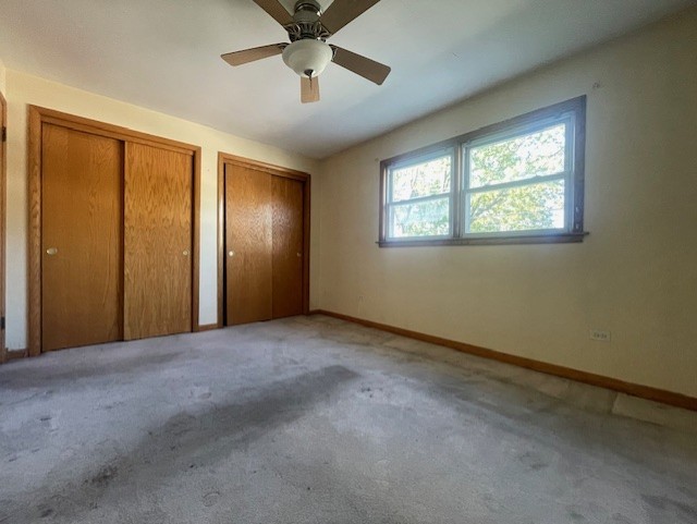 unfurnished bedroom featuring light carpet, ceiling fan, and multiple closets