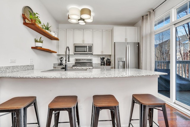 kitchen featuring a breakfast bar area, kitchen peninsula, white cabinets, and appliances with stainless steel finishes