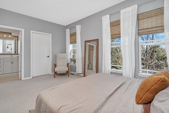 bedroom with multiple windows, connected bathroom, and light colored carpet