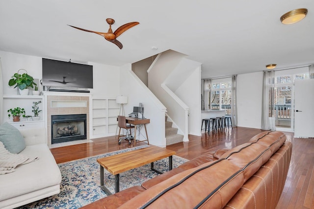 living room with a tile fireplace, wood-type flooring, and ceiling fan