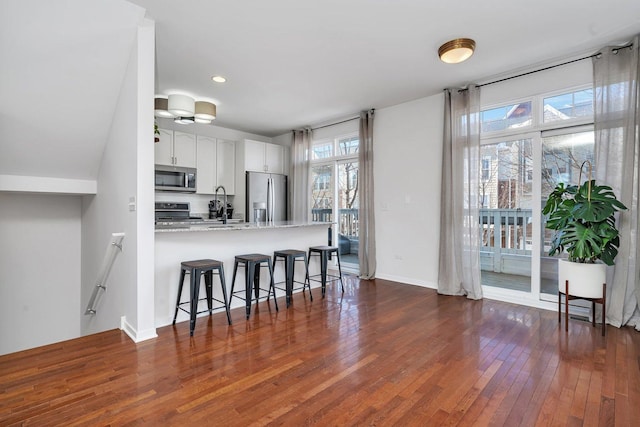 kitchen with white cabinetry, a kitchen bar, kitchen peninsula, stainless steel appliances, and plenty of natural light