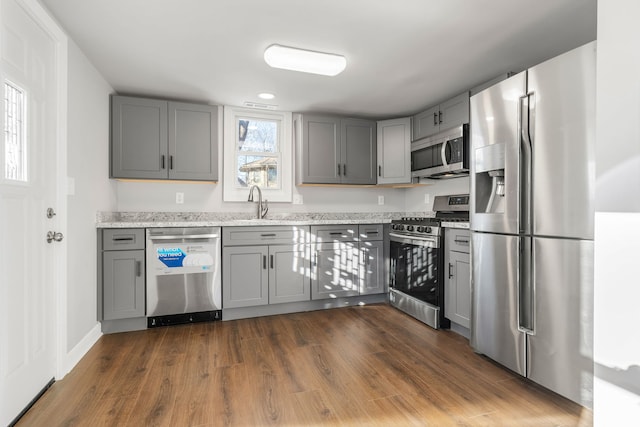 kitchen featuring light stone countertops, appliances with stainless steel finishes, dark wood-type flooring, sink, and gray cabinets