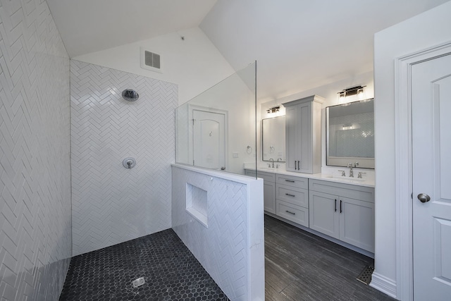 bathroom featuring lofted ceiling, wood-type flooring, vanity, and a tile shower