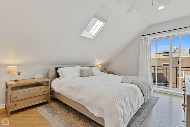 bedroom featuring hardwood / wood-style flooring, access to outside, lofted ceiling with skylight, and ceiling fan