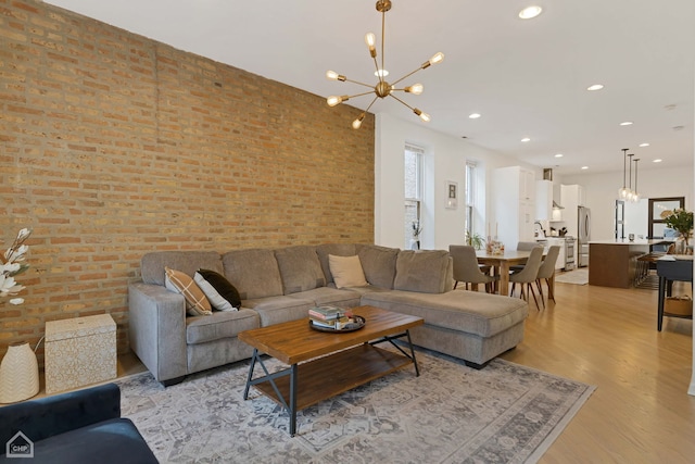 living room with brick wall, an inviting chandelier, and light hardwood / wood-style floors