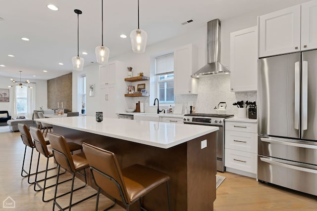 kitchen featuring a breakfast bar area, appliances with stainless steel finishes, white cabinets, a kitchen island, and wall chimney exhaust hood