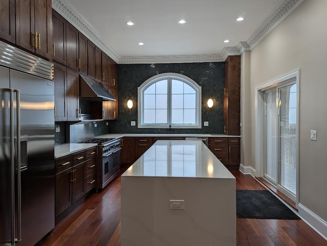 kitchen with backsplash, ornamental molding, premium appliances, dark wood-type flooring, and a center island