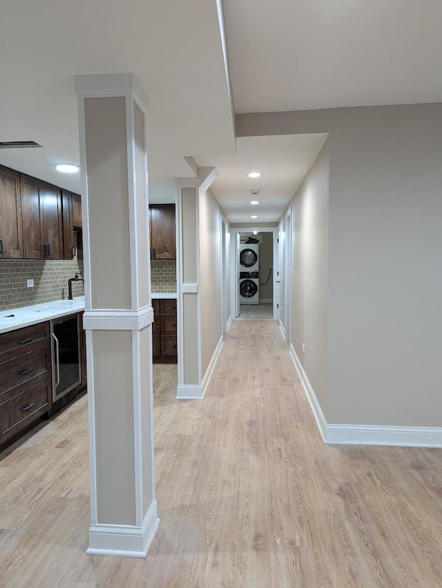 hallway featuring stacked washing maching and dryer, beverage cooler, and light hardwood / wood-style floors