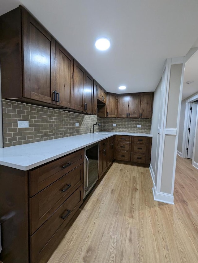 kitchen featuring decorative backsplash, dark brown cabinets, sink, light hardwood / wood-style floors, and wine cooler